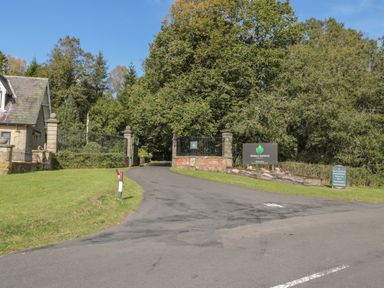 A driveway with gated entrance to Otterburn Hall Estate surrounded by trees and a stone building on the left at Treetops in Otterburn