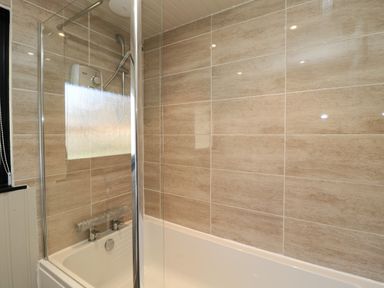 A bathroom with a bathtub shower area and tiled walls at Pine Tree in Otterburn