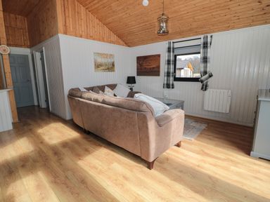 A living room with a corner sofa a coffee table a window with plaid curtains and wooden ceilings at Pine Tree in Otterburn