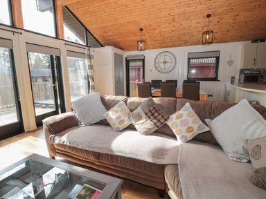 A living room with a sofa and cushions a dining table with chairs and large windows at Pine Tree in Otterburn