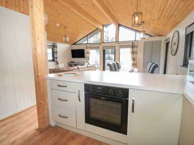 A kitchen with white cabinets and an oven overlooking a living area with a sofa and a dining table with chairs at Pine Tree in Otterburn