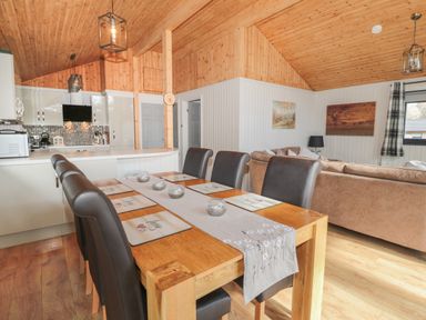 A dining area with a wooden table and six black chairs next to a kitchen and living room at Pine Tree in Otterburn