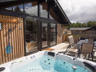 An outdoor deck area with a hot tub table and chairs attached to a wooden building at Pine Tree in Otterburn