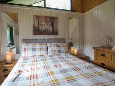A bedroom with a double bed with plaid bedding two bedside tables with lamps two mirrors and a chest of drawers at Pine Tree in Otterburn