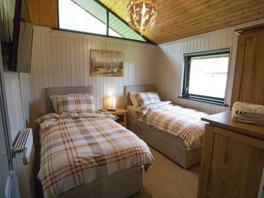 A bedroom with two single beds a nightstand with a lamp a wall painting a wooden wardrobe and a window at Pine Tree in Otterburn