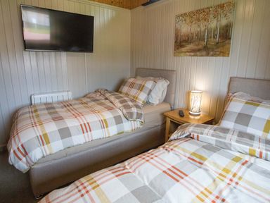 A bedroom with two single beds a nightstand with a lamp and remote and a wall-mounted television at Pine Tree in Otterburn