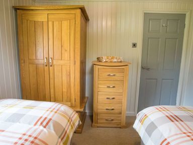 A bedroom with wooden wardrobe and chest of drawers between two beds at Pine Tree in Otterburn
