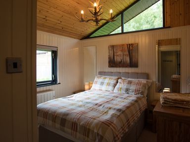 A bedroom with a double bed with plaid bedding a wooden ceiling antler chandelier and a window at Pine Tree in Otterburn