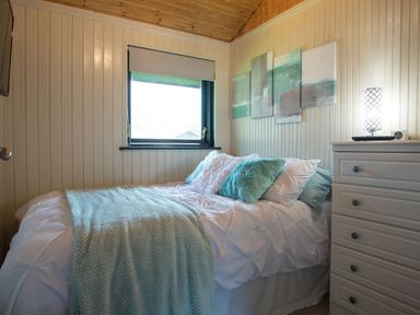 A bedroom with a bed with white and turquoise pillows a blanket a window and a white dresser with a lamp at Pine Tree in Otterburn