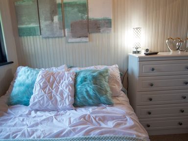 A bedroom with a bed with blue and white pillows and a white chest of drawers with a lamp and decorative hearts at Pine Tree in Otterburn