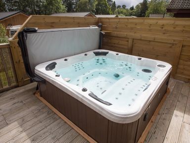 An outdoor hot tub with water and jets on a wooden deck with wooden fencing at Pine Tree in Otterburn