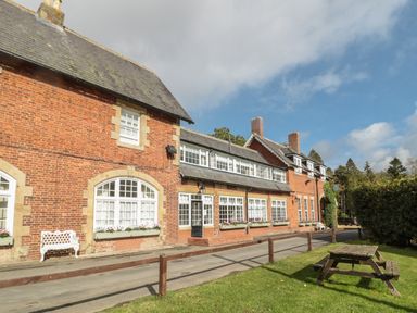 The exterior of a brick building with white framed windows a wooden bench a wooden picnic table and a grass lawn at Pine Tree in Otterburn