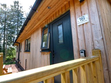Wooden exterior of lodge with black door and windows near wooden railing at Broken-Sky Lodge in Otterburn
