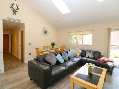 A living room with a black leather sofa and wooden dining table with chairs at Broken-Sky Lodge in Otterburn
