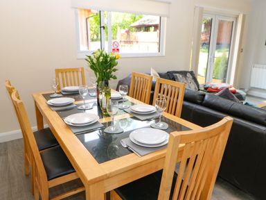 A dining table set with plates glasses and utensils next to a living area with a black sofa at Broken-Sky Lodge in Otterburn
