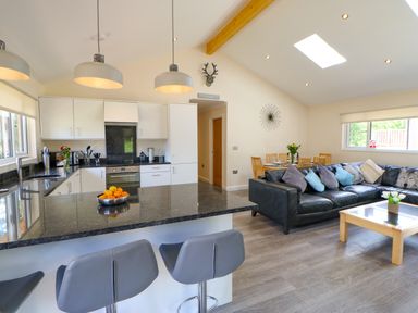 A kitchen with a black countertop island and bar stools next to a living area with a black sofa and dining table at Broken-Sky Lodge in Otterburn