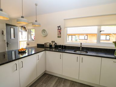 A kitchen with white cabinets black countertops a sink clock toaster kettle jars and hanging lights at Broken-Sky Lodge in Otterburn