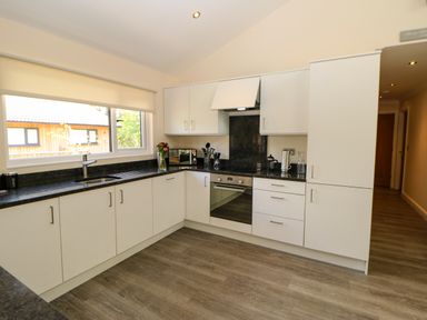 A kitchen with white cabinets black countertops a built-in oven a sink window and wooden flooring at Broken-Sky Lodge in Otterburn