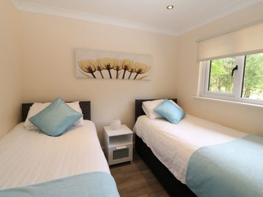 A bedroom with two single beds a nightstand and a window at Broken-Sky Lodge in Otterburn
