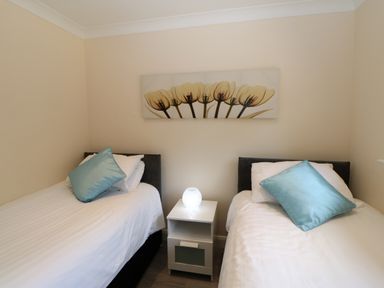 A bedroom with two single beds separated by a white nightstand and a light on it at Broken-Sky Lodge in Otterburn