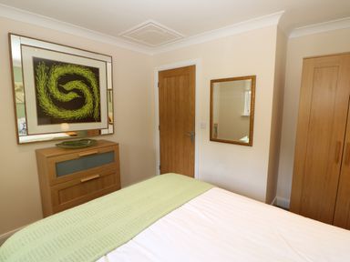 A bedroom with a bed, wooden dresser, wardrobe, wall mirror, and door at Broken-Sky Lodge in Otterburn