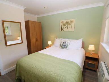 A bedroom with a bed green blanket bedside tables lamps wooden wardrobe and a mirror at Broken-Sky Lodge in Otterburn