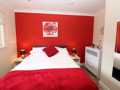 A bedroom with a bed against a red wall with red bedding and a white dresser at Broken-Sky Lodge in Otterburn