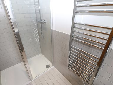 A bathroom with a glass shower enclosure and metal towel radiator at Broken-Sky Lodge in Otterburn