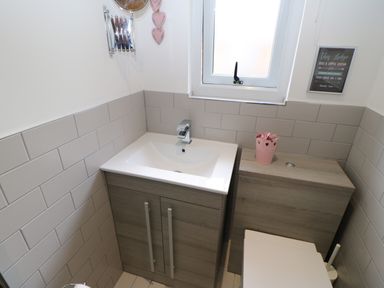 A bathroom sink unit and toilet with wooden cabinets and grey tiled walls at Broken-Sky Lodge in Otterburn
