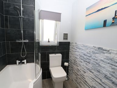 A bathroom with a bathtub shower combination a toilet and a window with a blind at Broken-Sky Lodge in Otterburn