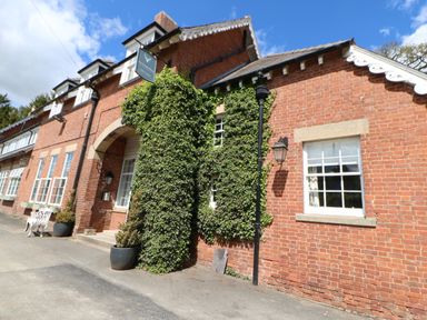 The exterior of a red brick building with ivy around the entrance and windows at Broken-Sky Lodge in Otterburn