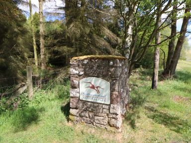 A stone sign for Northumberland National Park surrounded by grass and trees at Broken-Sky Lodge in Otterburn