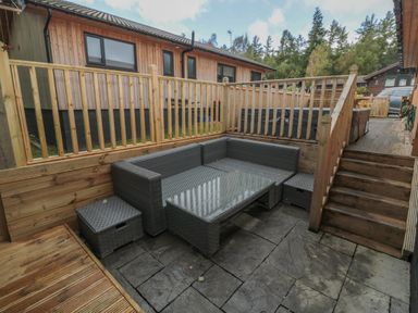 An outdoor seating area with a grey wicker corner sofa and table surrounded by wooden fencing and decking at Barn Owl in Otterburn