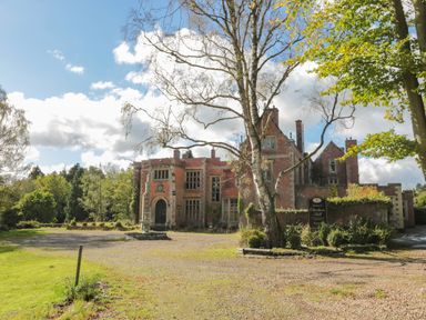 A gravel driveway leading to a large brick building with a fountain and trees at Otterburn Hall in Otterburn