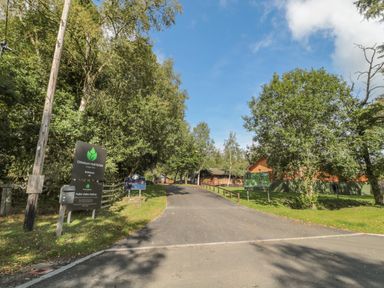 An entrance road lined with trees and signs leading to Otterburn Hall Estate Lodge Park in Otterburn