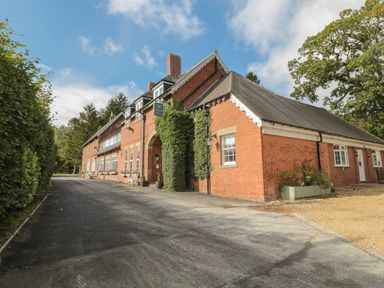 A red brick building with a driveway and greenery at Barn Owl in Otterburn