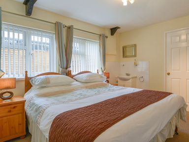 A bedroom with a double bed bedside tables lamps windows with curtains and vertical blinds and a washbasin at Broadclyst Cottage in Ottery St Mary