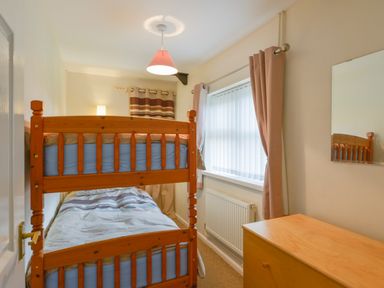 A bedroom with a wooden bunk bed a wooden chest of drawers and a window with curtains at Broadclyst Cottage in Ottery St Mary