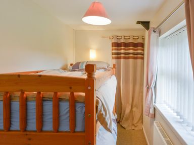 A bedroom with a wooden bunk bed striped curtains and window blinds at Broadclyst Cottage in Ottery St Mary