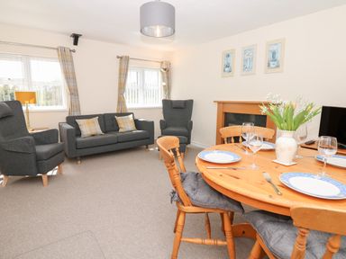 A living room with grey armchairs sofa and a wooden dining table set with plates glasses and a vase with flowers at Broadclyst Cottage in Ottery St Mary