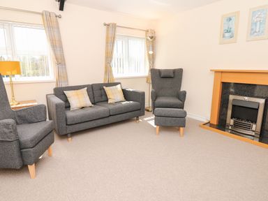 A living room with grey sofas a fireplace and yellow curtains at Broadclyst Cottage in Ottery St Mary