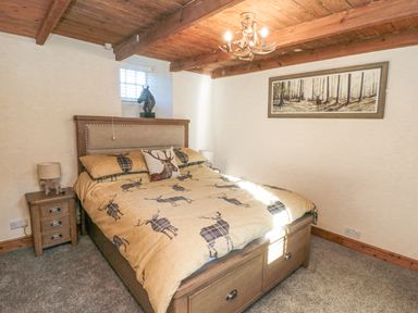A bedroom with a bed and nightstand under wooden ceiling beams at The Nook at 29 High Street Cloughton near Burniston