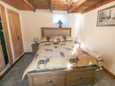 A bedroom with a bed featuring deer patterned bedding two bedside tables with lamps wooden ceiling and doors and a small window at The Nook at 29 High Street Cloughton near Burniston