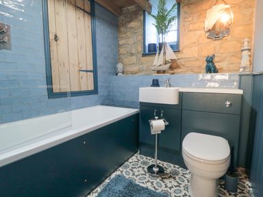 A bathroom with a bathtub toilet sink blue cabinets and patterned floor tiles at The Nook at 29 High Street in Cloughton near Burniston