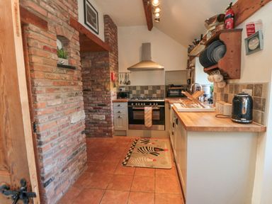 A kitchen with tiled floor wooden countertops and brick walls with shelves holding plates and cups at The Nook at 29 High Street Cloughton near Burniston