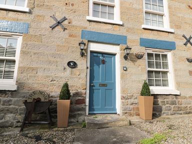 A front entrance with a blue door flanked by two plants in pots at The Nook at 29 High Street Cloughton near Burniston