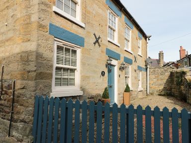 A stone house with blue window shutters a blue door fenced front yard and two potted plants at The Nook at 29 High Street Cloughton near Burniston