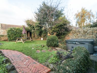 A garden with a wooden picnic table and umbrella a hot tub a brick pathway and stone wall at The Nook at 29 High Street Cloughton near Burniston