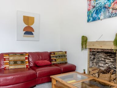 A red leather sofa with patterned cushions next to a stone fireplace with wood and pine cones at Barwood View in Torquay