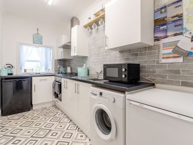 A kitchen with white cabinets black countertop and patterned floor at Barwood View in Torquay